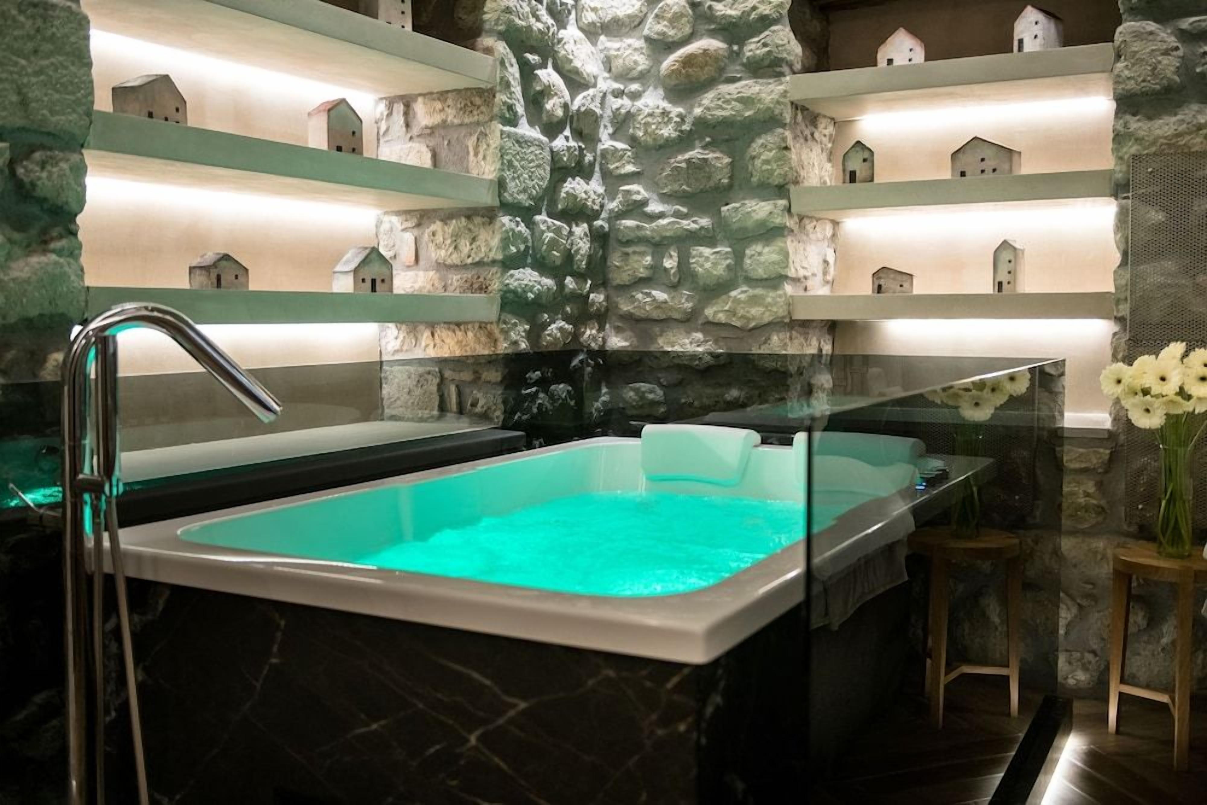Un área de spa con una bañera grande, paredes de piedra y estantes con objetos decorativos.