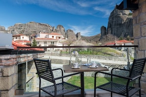 Un balcón con dos sillas y una mesa, con vista a un valle de formaciones rocosas y edificios.