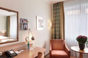 Una habitación de hotel con escritorio, teléfono, lámpara, silla y un espejo grande.