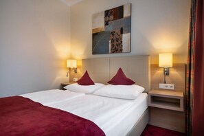 A hotel room with a bed, two bedside lamps, a nightstand, a wall-mounted artwork, and a red curtain. - Select Hotel Tiefenthal (Hamburg)