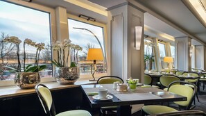 A restaurant with tables, chairs, potted orchids, and a view of the city. - Select Hotel Tiefenthal (Hamburg)