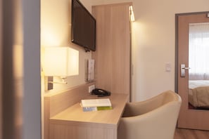 Ein Hotelzimmer mit Schreibtisch, Stuhl, Bett, Fernseher und Nachttisch.