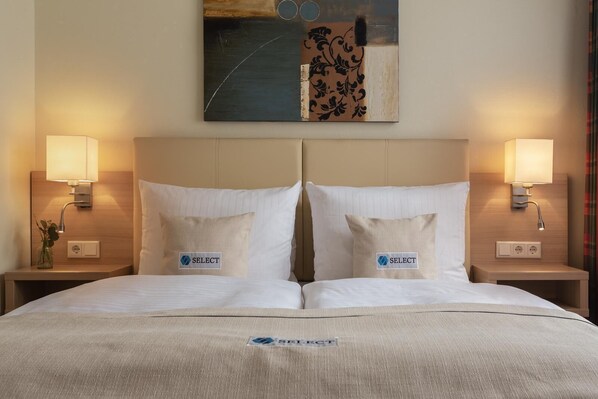 Una habitación de hotel con una cama grande, dos mesitas de noche, dos lámparas y un cuadro en la pared.