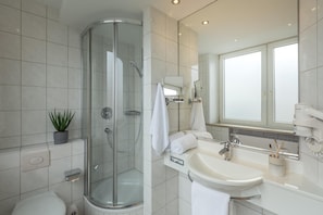 Ein modernes Badezimmer mit einer Duschkabine aus Glas, einem Waschbecken mit Spiegel und einer Topfpflanze.
