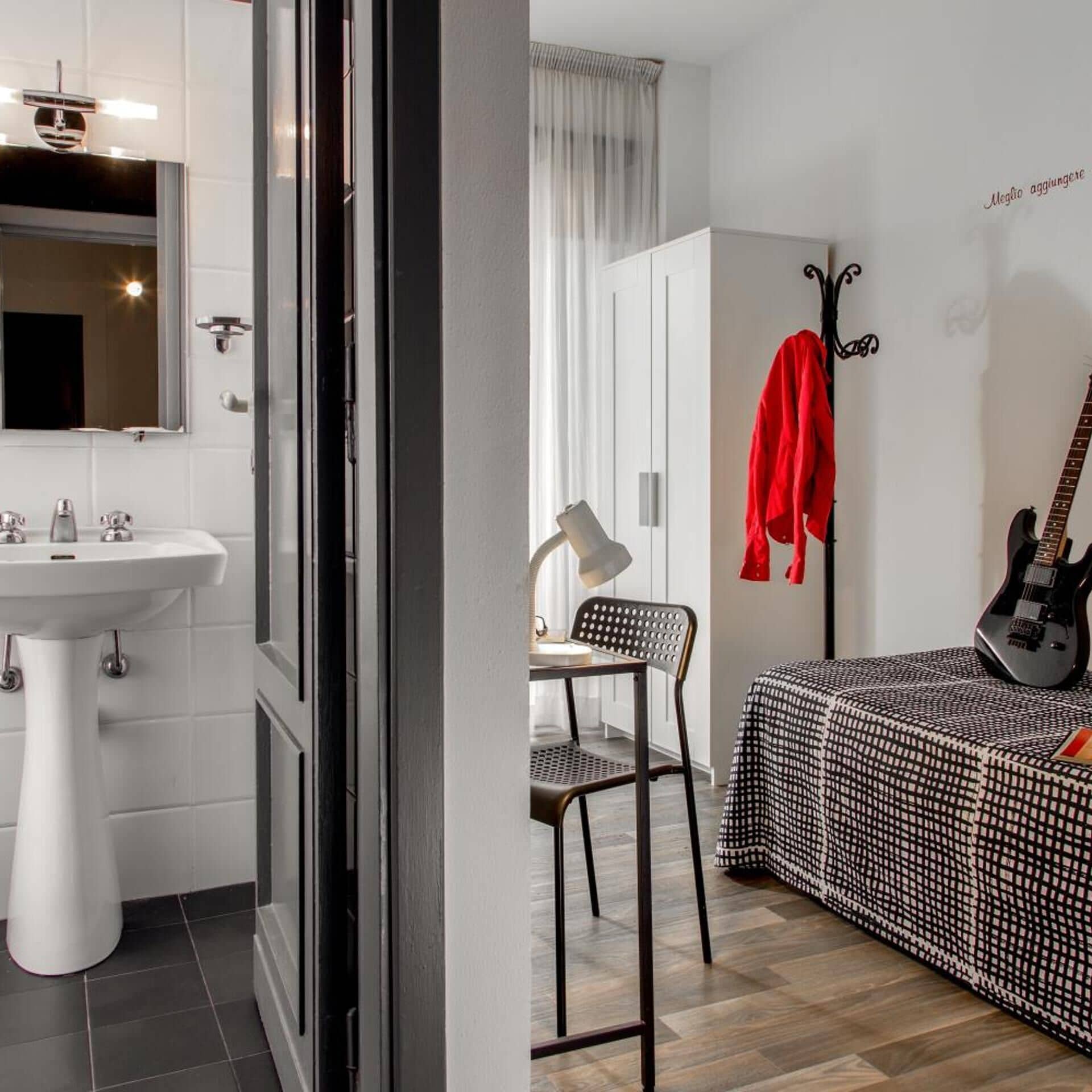 A modern bathroom with a white sink and mirror, a wooden floor, and a bed with a patterned bedspread.