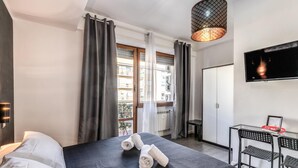 A hotel room with a bed, a desk, a chair, a TV, and a view of the outside. - Radio Hotel (Rome)