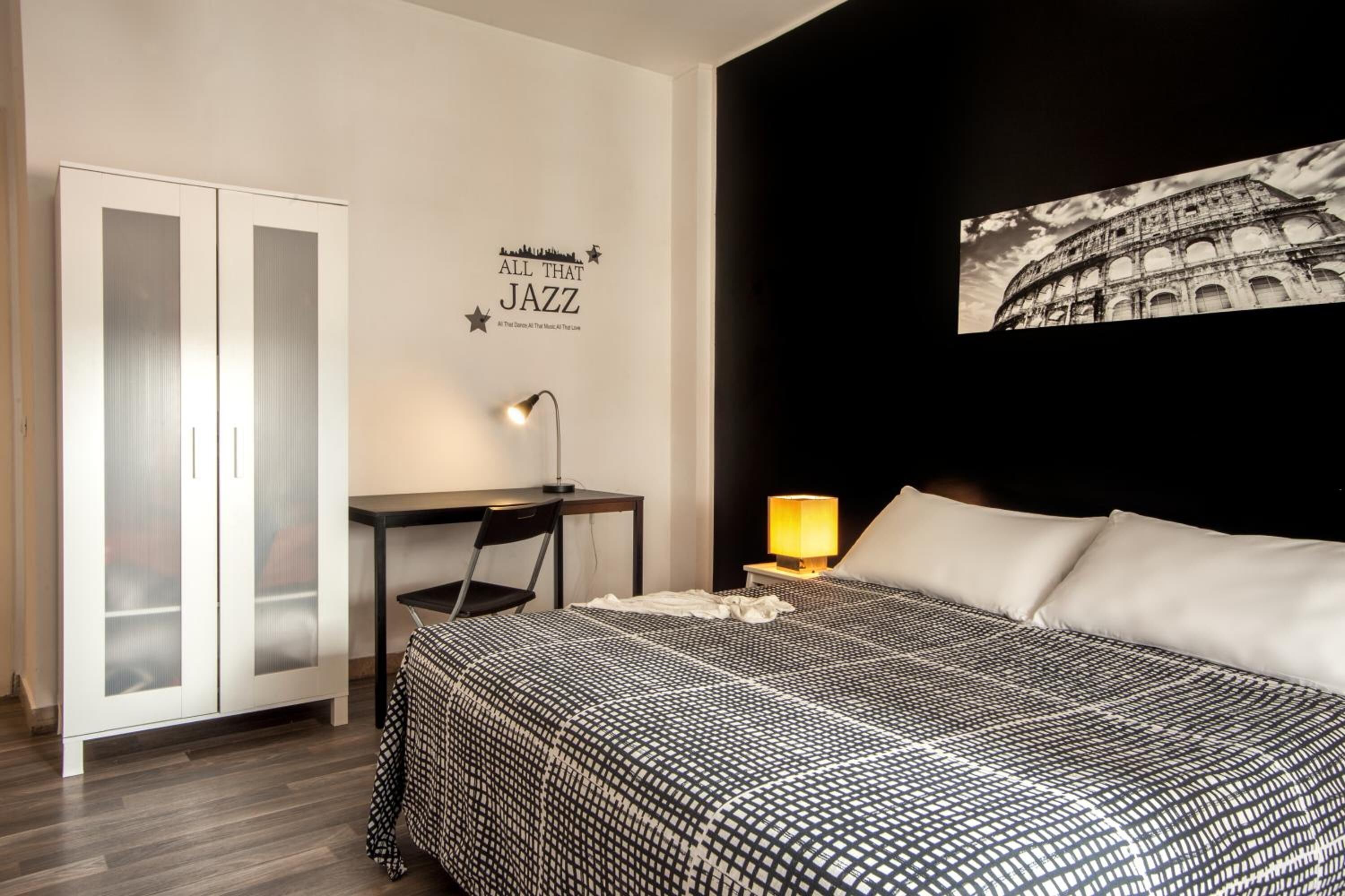 A bedroom with a bed, a desk, a chair, a wardrobe, and a wall with a picture and text.