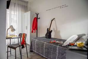 Ein Schlafzimmer mit einem Bett, einer Gitarre, einem Stuhl, einem Tisch mit Gläsern und einer Lampe.