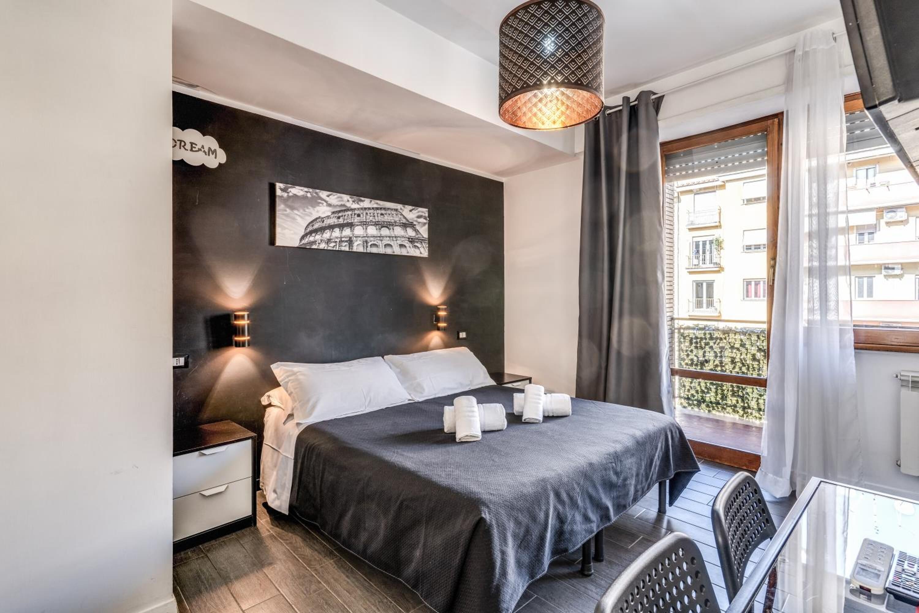 Une chambre à coucher comprenant un lit, des tables de chevet, un tableau accroché au mur, un balcon avec vue et un luminaire suspendu.