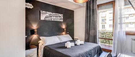 Une chambre à coucher comprenant un lit, des tables de chevet, un tableau accroché au mur, un balcon avec vue et un luminaire suspendu.