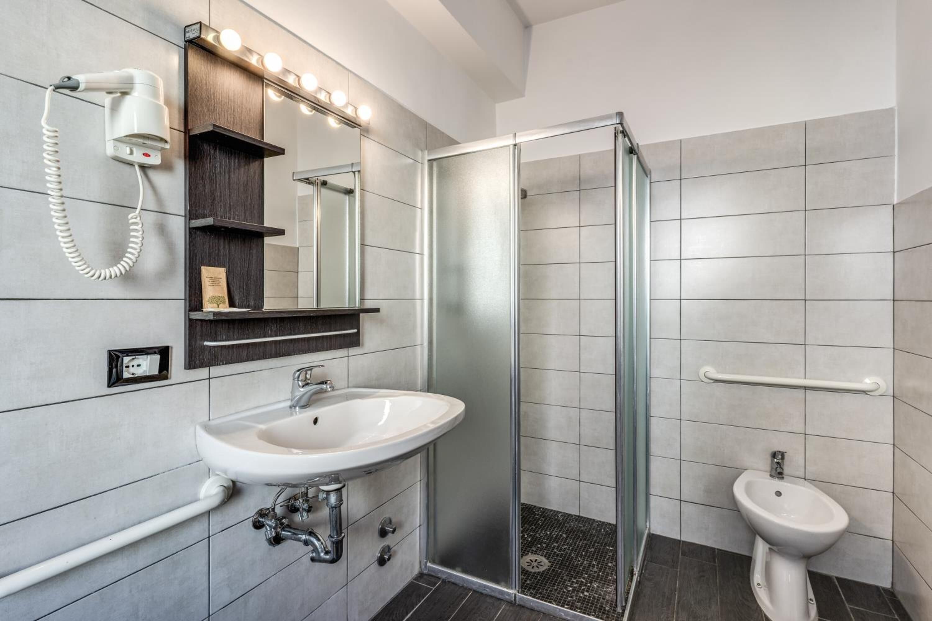 Un baño moderno con cabina de ducha de vidrio, lavamanos pedestal, tocador con espejo y bidé.