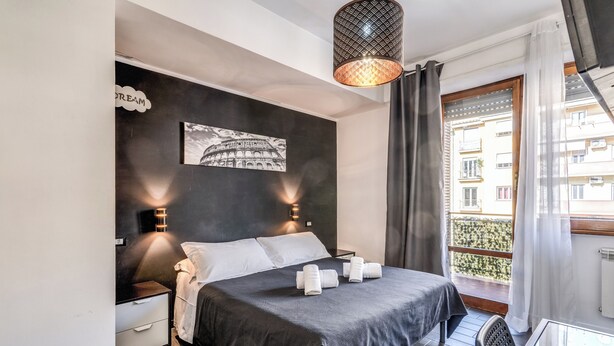 A bedroom with a bed, bedside tables, a wall-mounted picture, and a balcony with a view. - Radio Hotel (Rome)