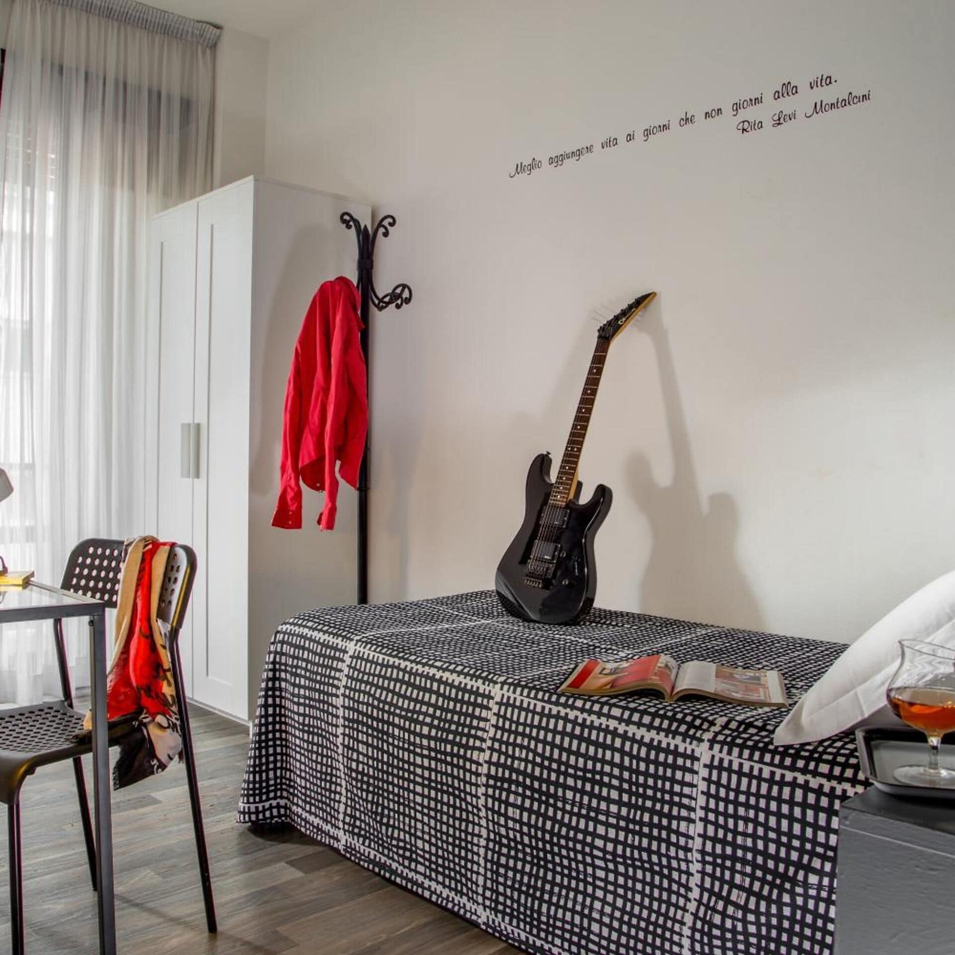 Una habitación con una cama, una guitarra, una silla, una mesa y una pared con una cita.