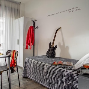 A room with a bed, a guitar, a chair, a table, and a wall with a quote. - Radio Hotel (Rome)