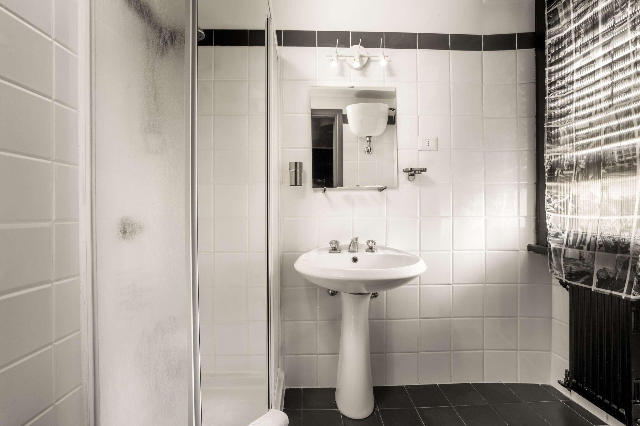 A bathroom with a white sink, a mirror, and a shower enclosure.