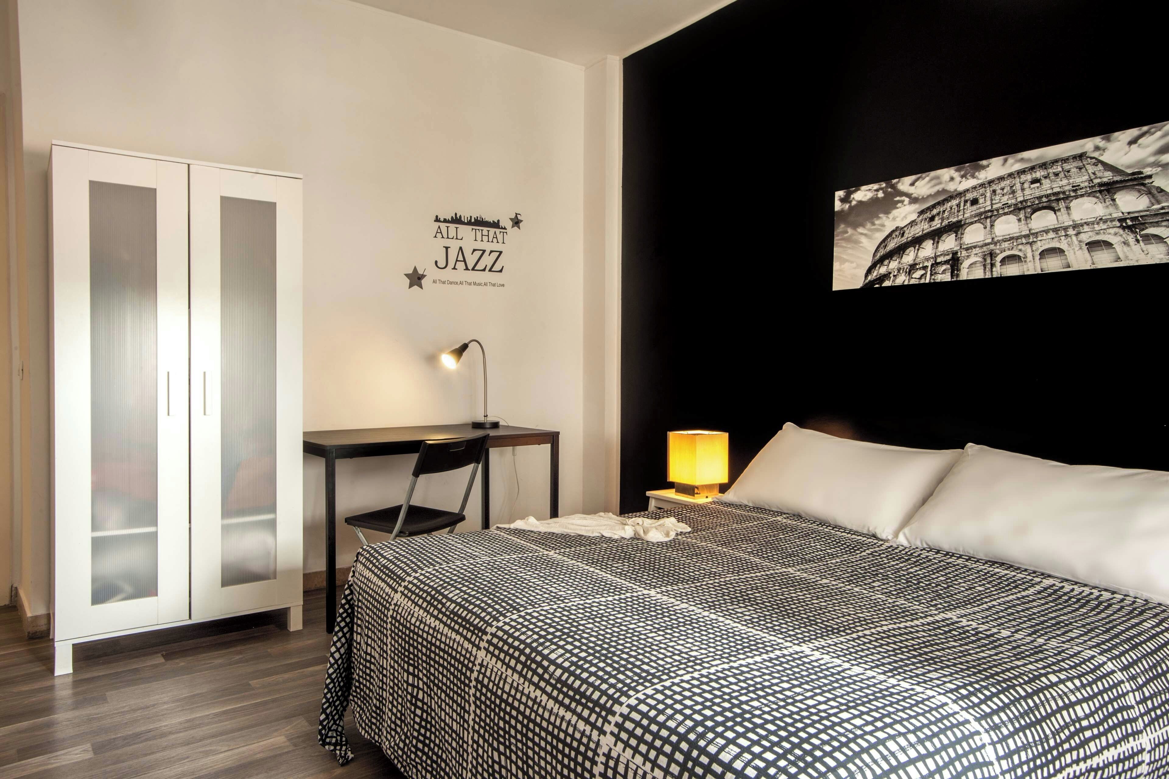 Hotelkamer met een bed, een bureau, een kledingkast en een muur met een stadsbeeld en een afbeelding van het Colosseum.