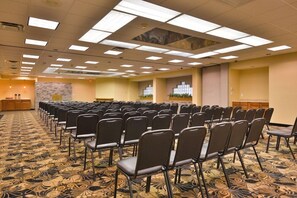 Une salle de conférence avec des rangées de chaises, un sol recouvert de moquette et un plafond doté de luminaires carrés.