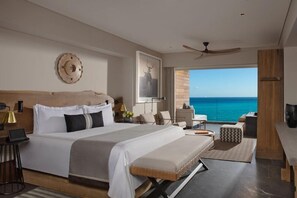 A modern hotel room with a large bed, a desk, a chair, a view of the ocean, and a ceiling fan. - Impression Moxché by Secrets Adults Only (Playa del Carmen)