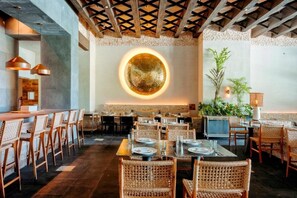 A restaurant with a central circular light feature, wooden chairs, and tables set for dining. - Impression Moxché by Secrets Adults Only (Playa del Carmen)