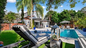 Ein Garten mit Swimmingpool, Liegestühlen und Grill.