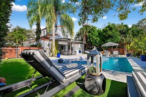 Ein Garten mit Swimmingpool, Liegestühlen und Grill.