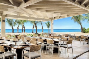 An outdoor dining area with tables and chairs, overlooking a beach with palm trees and the ocean. - Sunscape Dominicus La Romana (San Rafael del Yuma)