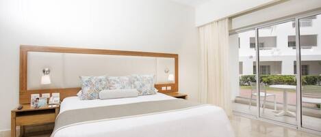 A hotel room with a large bed, a nightstand with a lamp, a window with a view of the outside, and a balcony with a table and chairs.