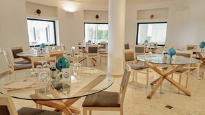 A hotel dining area with round glass tables, wooden chairs, and large windows. - Sunshine Club Hotel & Spa (Ricadi)