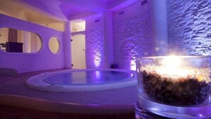 A room with a stone wall, a circular seating area, and a glass table with a candle. - Sunshine Club Hotel & Spa (Ricadi)