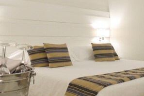 Hotellihuone, jossa on sänky, tyynyjä, yöpöytälamppu ja metallinen ämpäri.