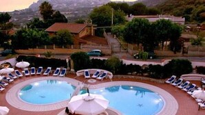 A pool area with two circular pools, lounge chairs, umbrellas, and a view of the surrounding landscape. - Sunshine Club Hotel & Spa (Ricadi)