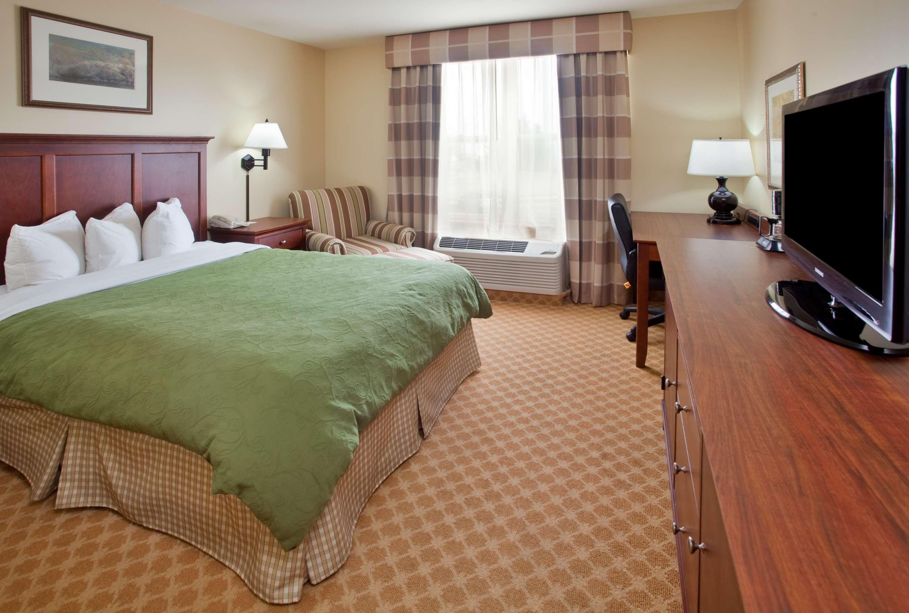 A hotel room with a large bed, a desk, a television, and a window with curtains.