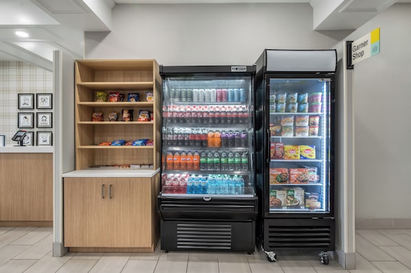 A vending machine with various snacks and drinks, a refrigerated display case with frozen foods, and a shelf with packaged goods. - Garner Hotel Birch Run - Frankenmuth Area by IHG (Birch Run)