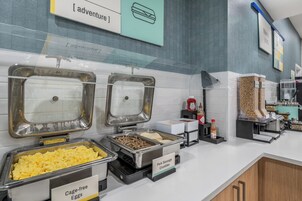Zona de buffet con opciones de comida identificadas, incluyendo huevos, salchicha y una sección señalizada como 'adventure'.