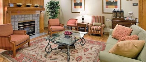 A living room with a fireplace, two armchairs, a sofa, a glass coffee table, and a rug.