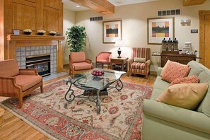 A living room with a fireplace, two armchairs, a sofa, a glass coffee table, and a rug. - Country Inn & Suites by Radisson, Birch Run-frankenmuth, MI (Birch Run)