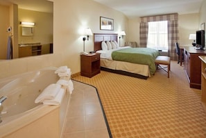 A hotel room with a large bathtub, a bed with a green bedspread, a desk with a computer, and a television.