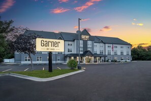 Hotel amb un cartell que diu 'Garner BY IHG' davant d'un edifici amb una plaça d'aparcament.