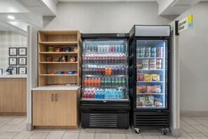 Ein Getränkeautomat mit verschiedenen Snacks und Getränken, ein Kühlregal für Tiefkühlkost sowie eine Ablage mit verpackten Waren.