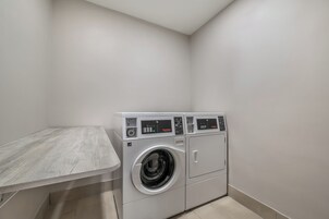 Un lavadero con lavadora y secadora, una mesita pequeña y una pared lisa.