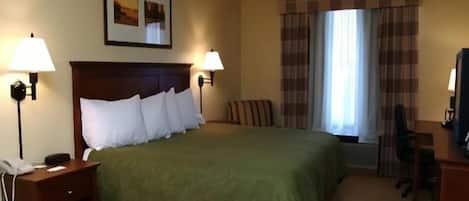Une chambre d’hôtel avec un grand lit, deux lampes de chevet, un bureau avec une chaise, un téléphone et une fenêtre avec des rideaux.