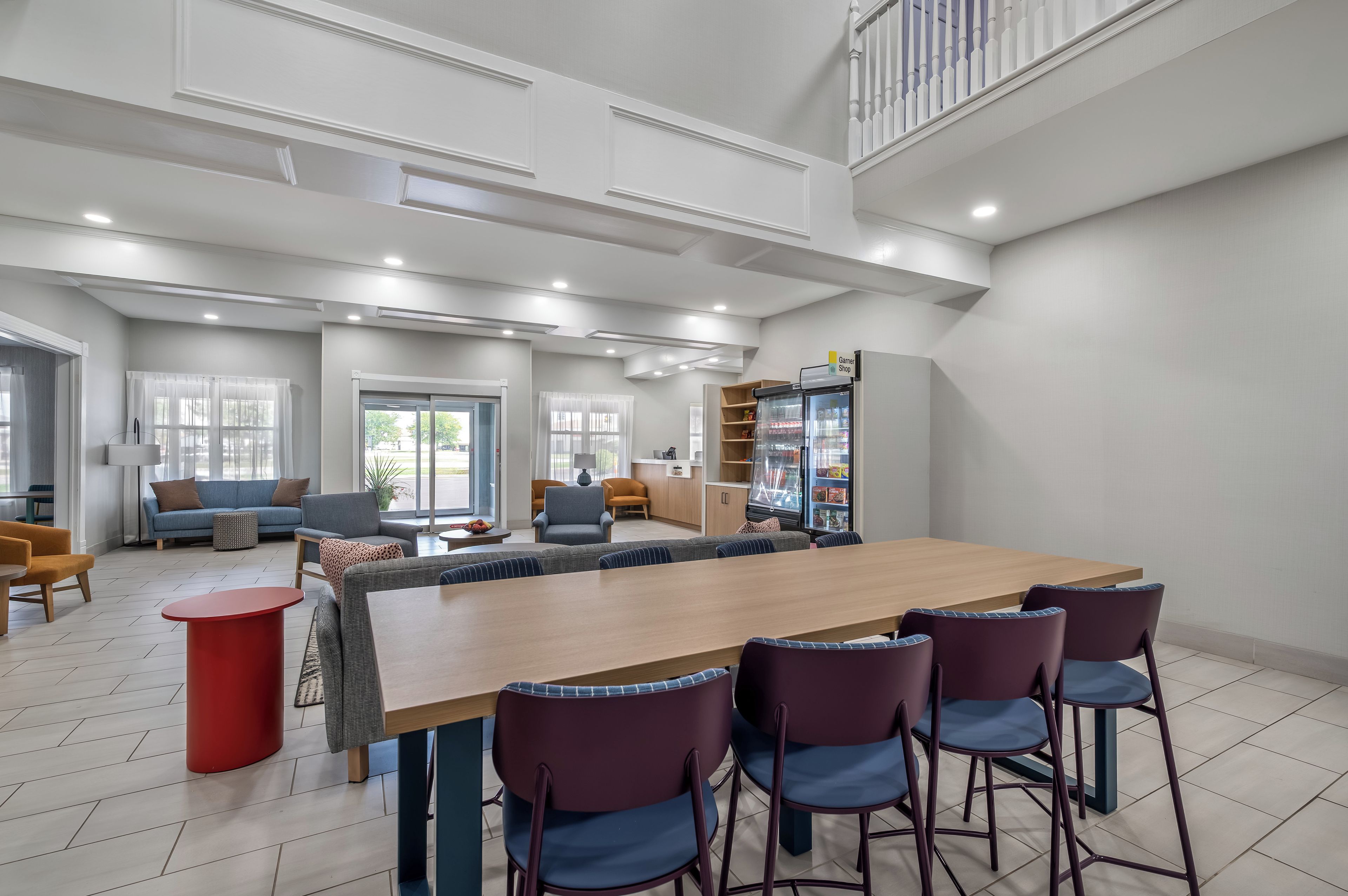 A spacious living area with a long wooden table, multiple chairs, a sofa, and a kitchen area with a refrigerator.