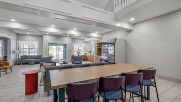 A spacious living area with a long wooden table, multiple chairs, a sofa, and a kitchen area with a refrigerator.
