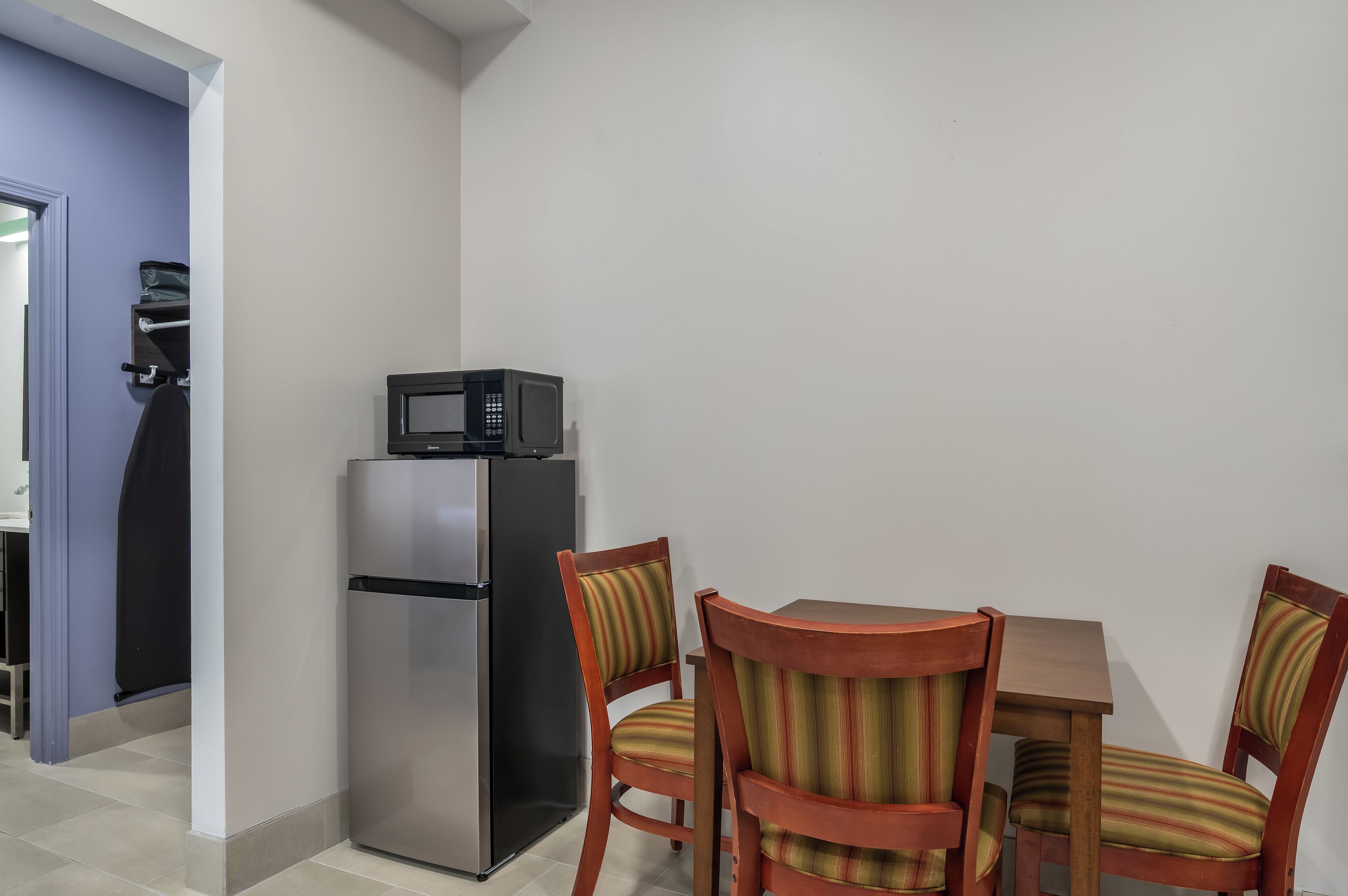 A compact kitchen with a refrigerator, microwave, and a small dining table with chairs.