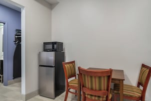 Cocina compacta con refrigerador, microondas y una pequeña mesa de comedor con sillas.