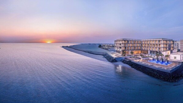Ein Hotel am Wasser mit modernem Design, das einen Poolbereich und einen Sonnenuntergang bietet.