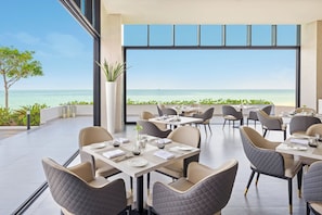 A modern restaurant with tables and chairs arranged on a terrace overlooking the sea. - Beach Bay Hotel Mirfa, Edge by Rotana (Al Mirfa)
