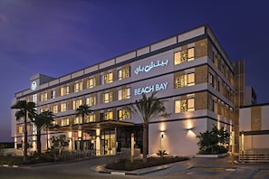 A multi-story hotel with a modern facade, illuminated signage, and palm trees in the foreground. - Beach Bay Hotel Mirfa, Edge by Rotana (Al Mirfa)