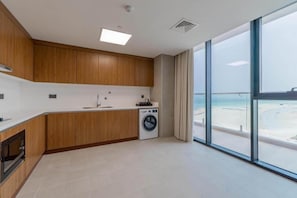 A modern kitchen with wooden cabinets, a washing machine, and a large window with a beach view. - Beach Bay Hotel Mirfa, Edge by Rotana (Al Mirfa)