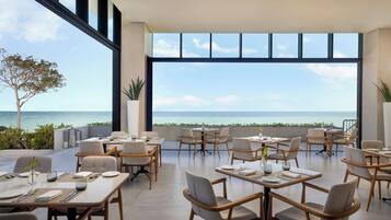A restaurant with tables and chairs, a view of the ocean, and potted plants.